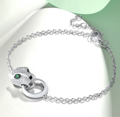 Narrow 925 silver bracelet with plastic 3D panther or leopard head made of clear zirconia. Green stones and black spinel for eyes and nose. The big cat holds a silver ring between its teeth.https://spoo-design.de/en/product/5954/